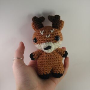 a crochet deer in a hand with a white background