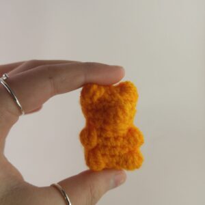 a orange crochet gummy bear in a hand with a white background
