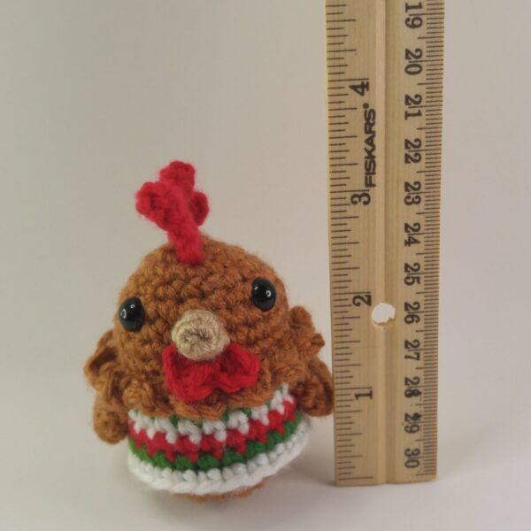 A crochet Christmas chicken beside a ruler with a white background
